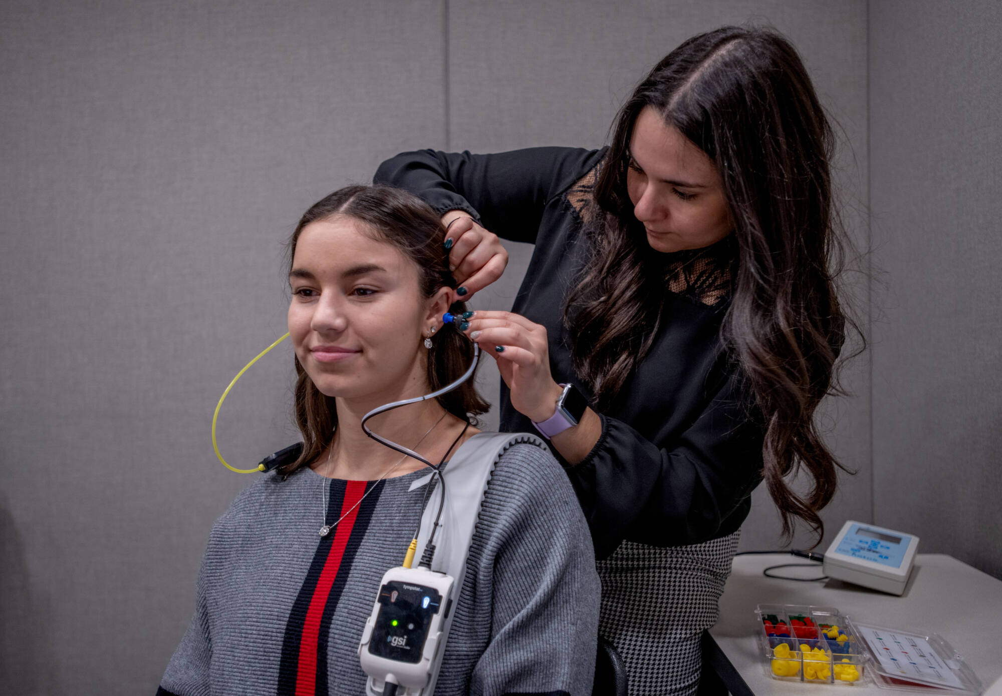 Two students practice adjusting an audio medical device on each other